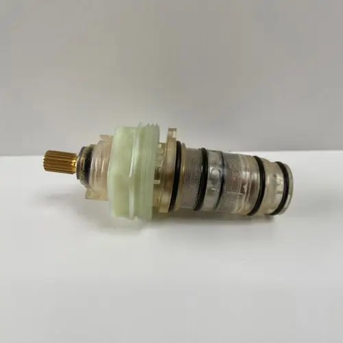 Ideal Standard Thermostat-Kartusche mit transparentem Gehäuse und unterschiedlichen Dichtungsringen, mechanischer Verstellmechanismus, auf weißem Hintergrund.